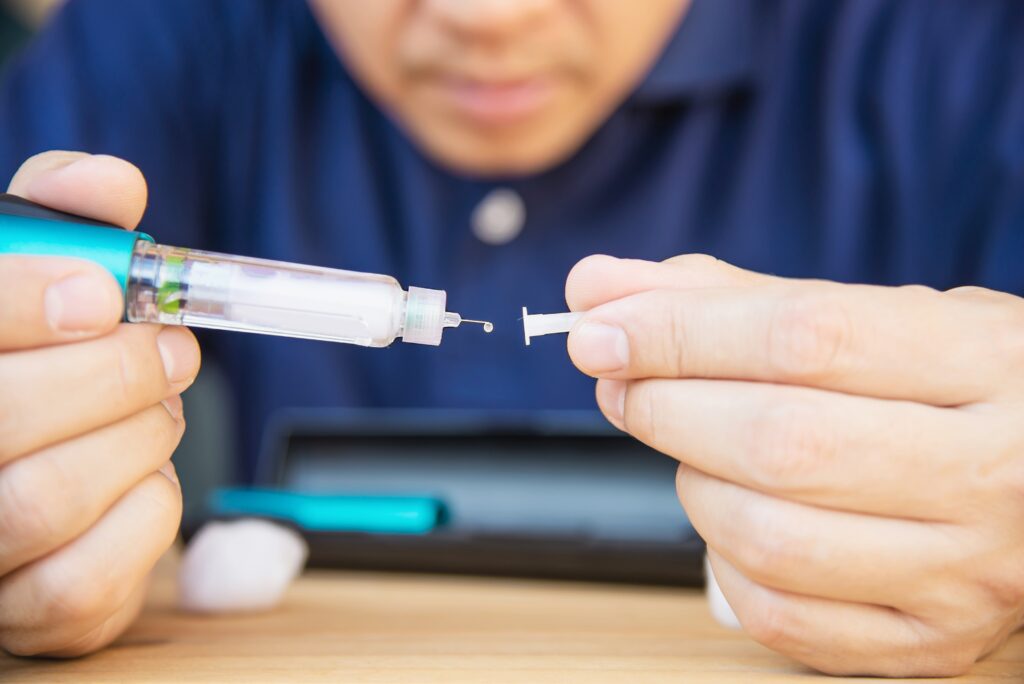 Close-up of a man preparing an insulin syringe with a tablet in the background.