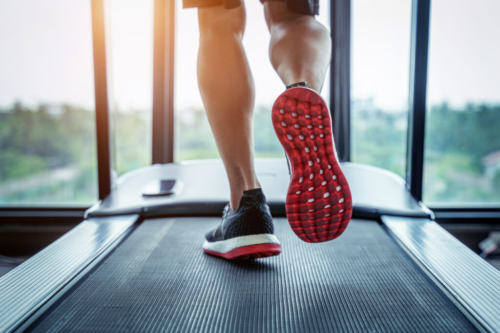 Close-up of a person's feet running on a treadmill, showcasing the red sole of the shoe, with a scenic window view in the background.