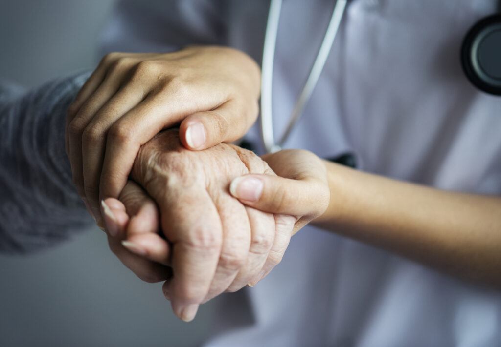 Close-up of a medical professional's hand gently holding an elderly patient's hand, symbolizing care and compassion