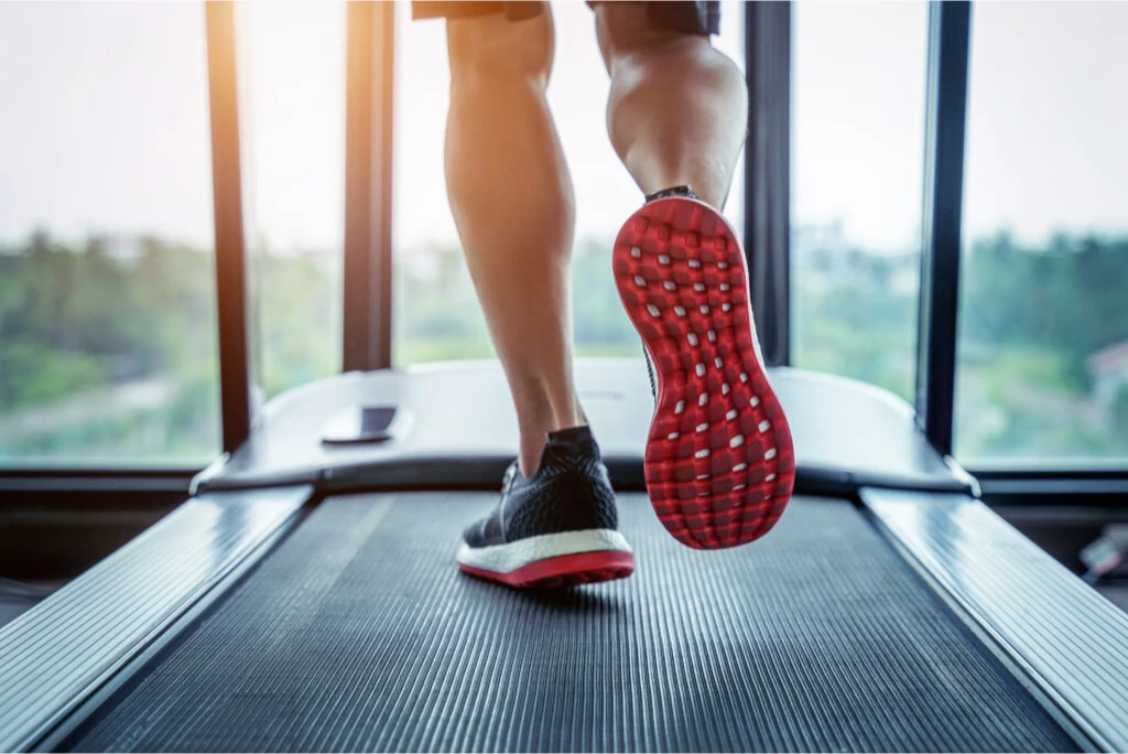 Person running on a treadmill with a focus on red-soled shoes.