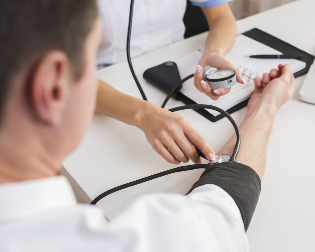 Close-up of a medical professional measuring a patient's blood pressure with a sphygmomanometer on a table with medical notes and equipment.