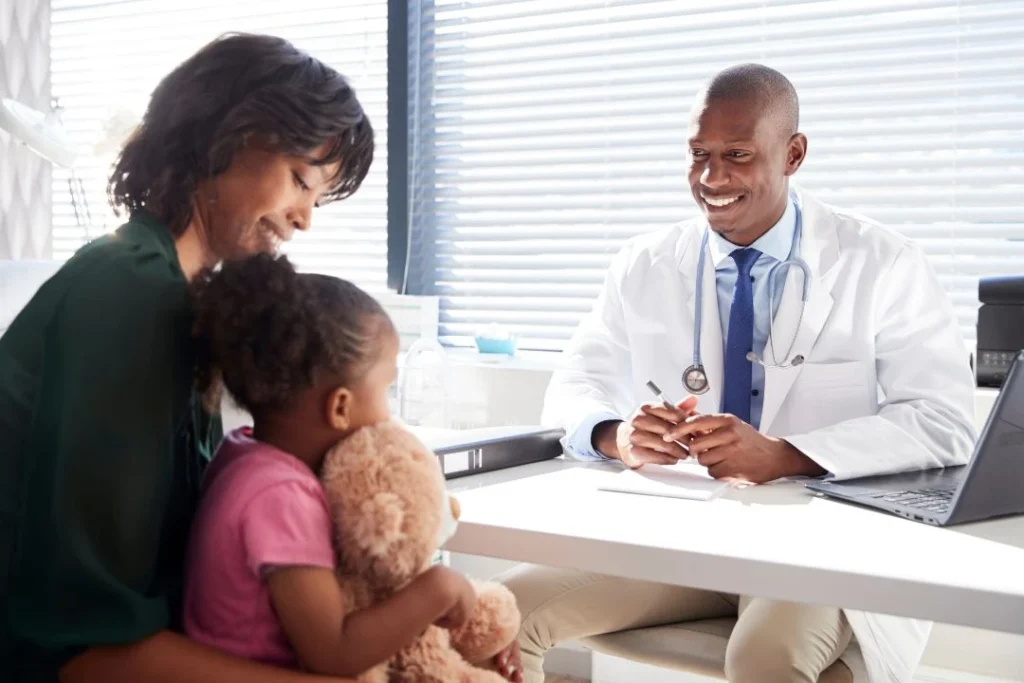 A happy doctor discusses with a mother holding her child in a sunny clinic.