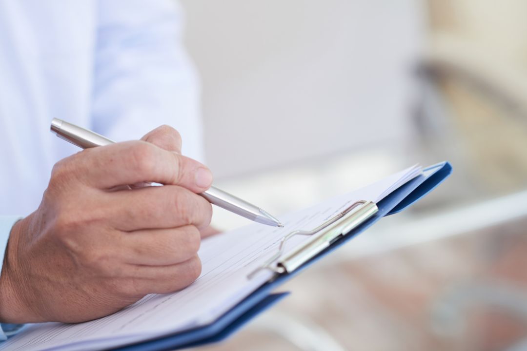 Close-up of hand writing on medical clipboard.
