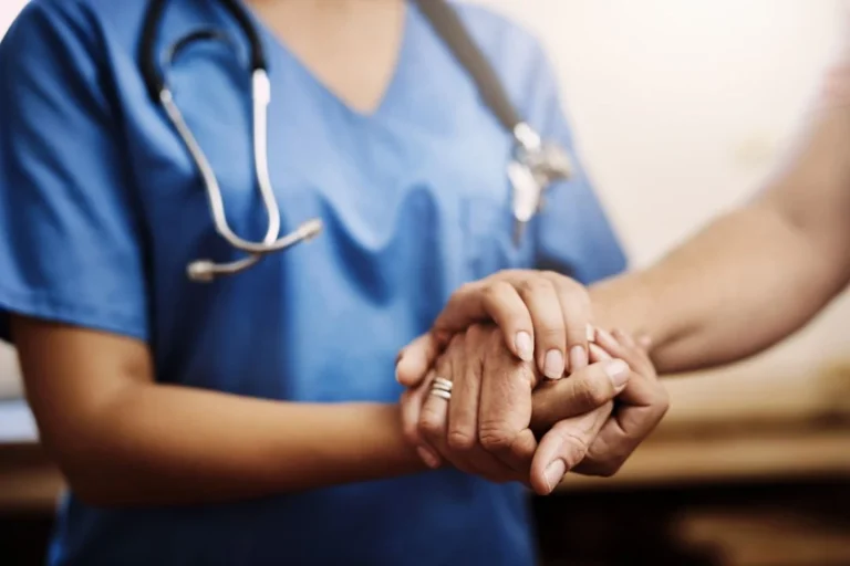 Healthcare worker in scrubs holding a patient's hand.