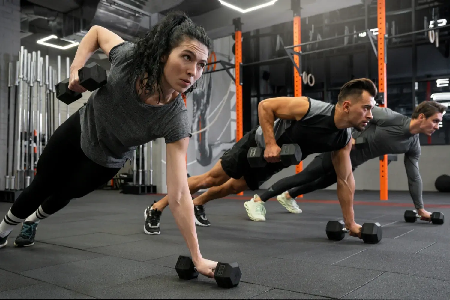 A group of people doing strength training exercises using dumbbells at a gym.