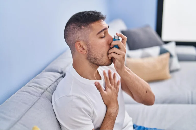 A man sitting on a couch using an asthma inhaler.