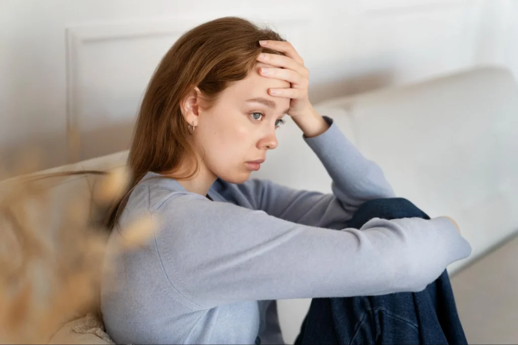 A woman sitting on a couch with her hand on her forehead, looking stressed.