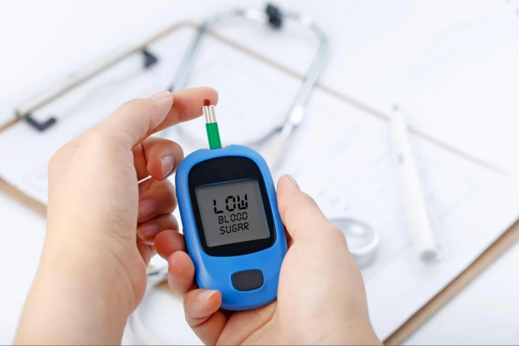 A hand holding a glucose meter with a "Low Blood Sugar" reading displayed.