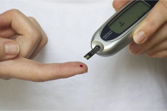 A close-up of a person's finger with a drop of blood being tested using a glucose meter.