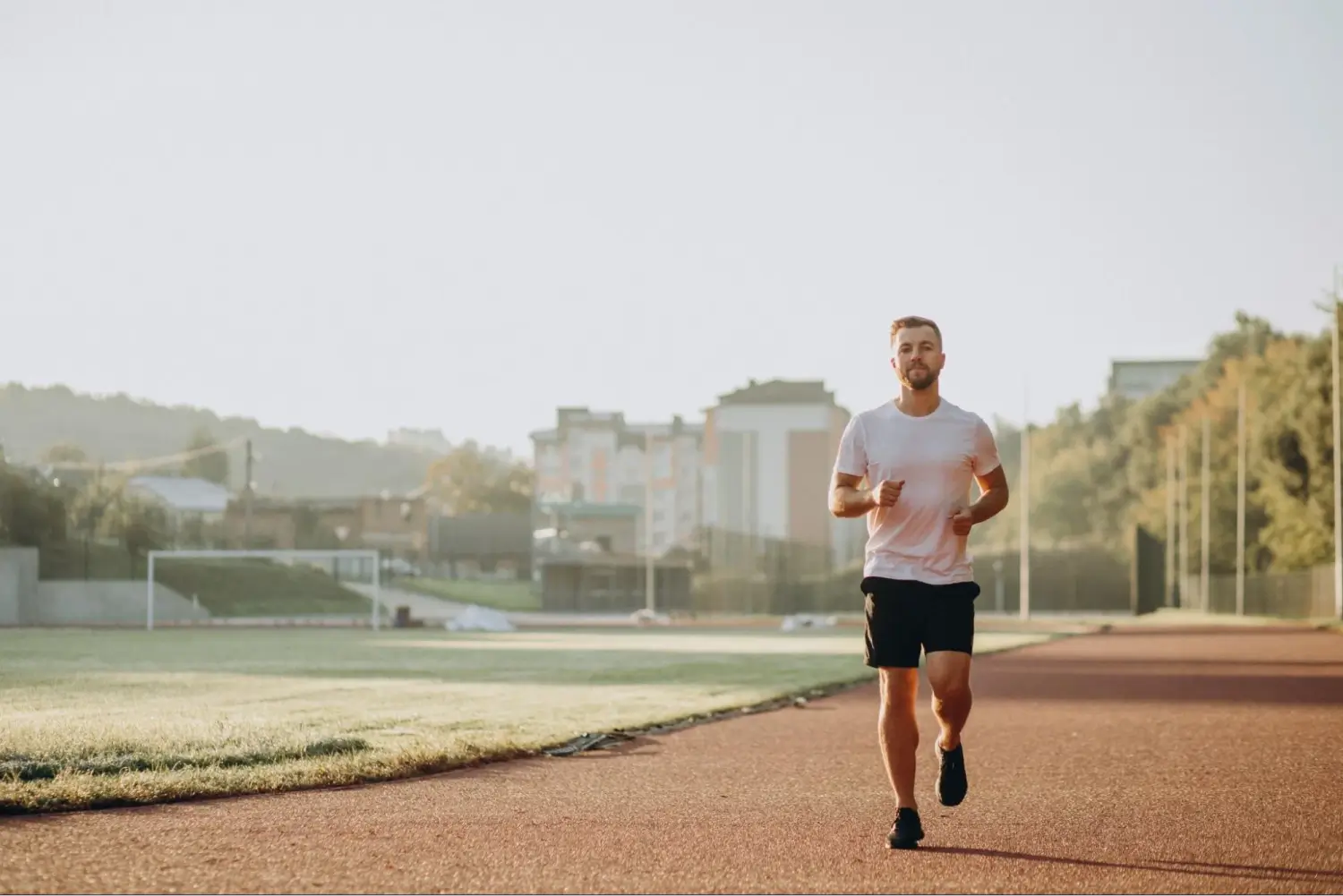 A man running on an outdoor track with buildings and greenery in the background.