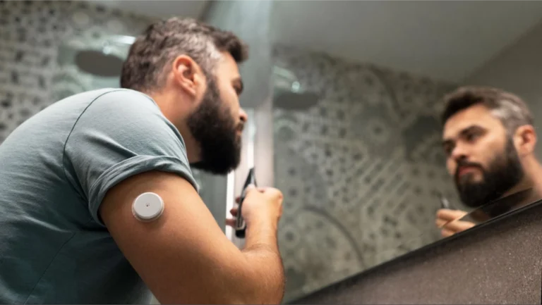 A man looking at himself in a mirror with a glucose sensor attached to his arm.