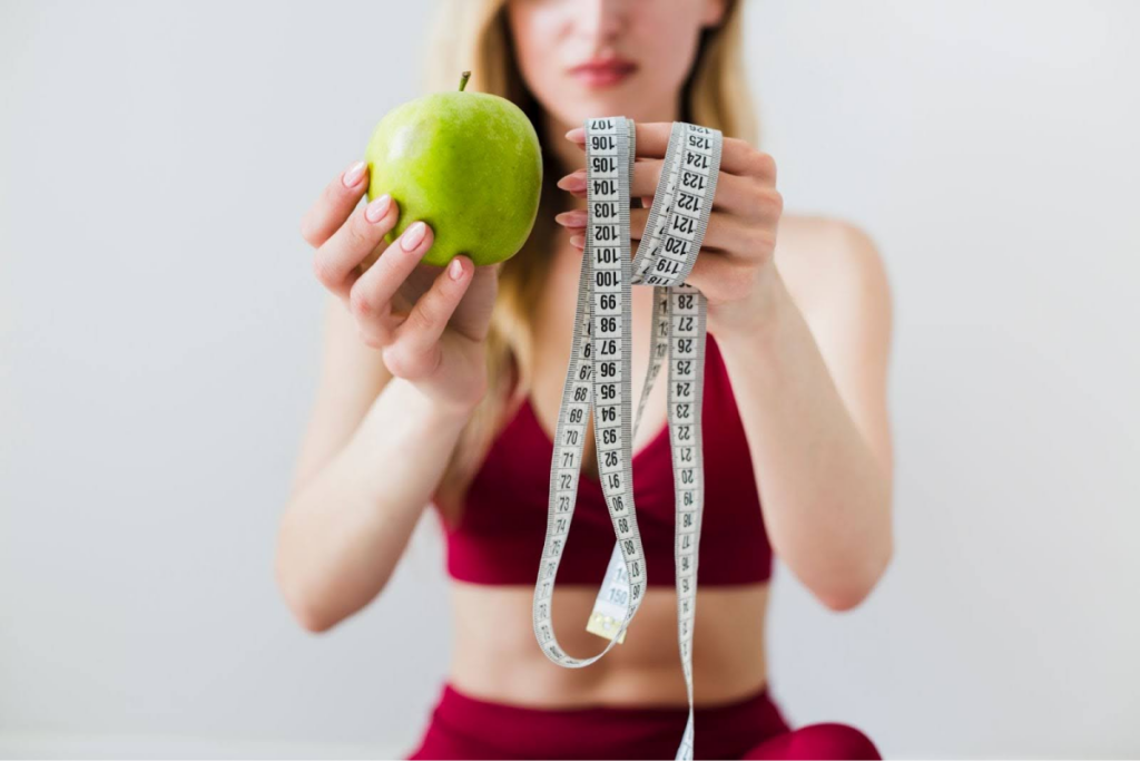 A woman holding a green apple and a measuring tape, symbolizing health and fitness.