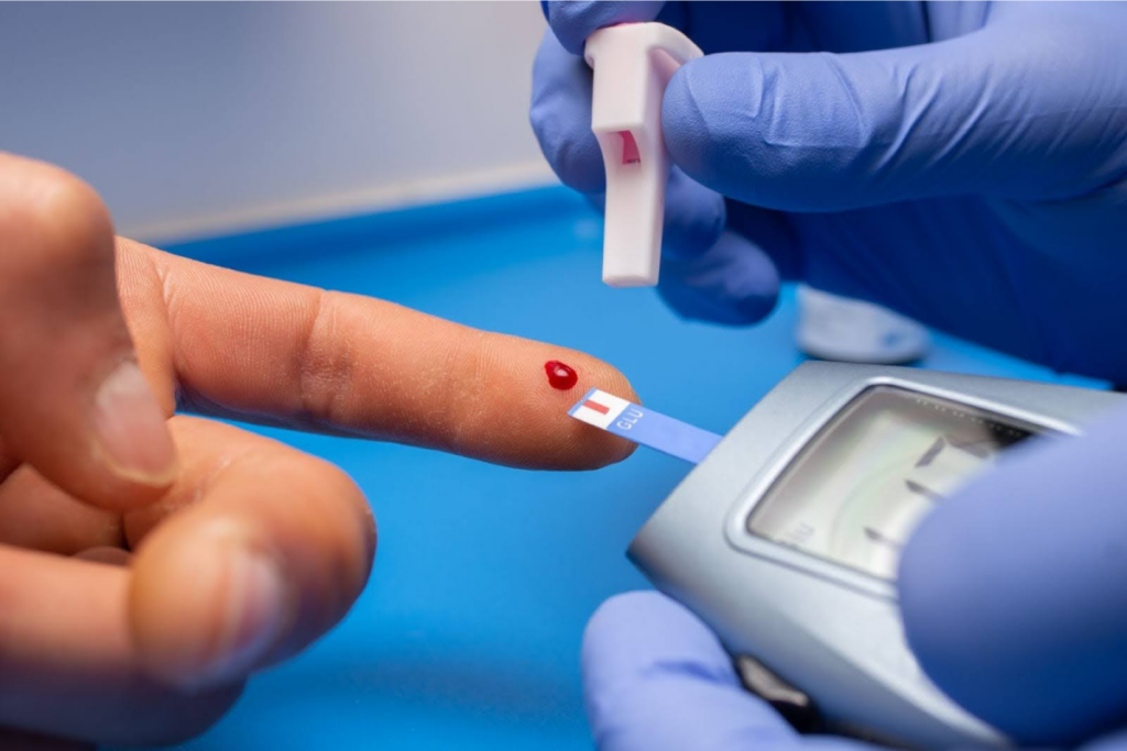 A close-up of a finger prick and a glucometer strip with a drop of blood.