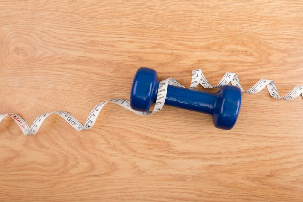 A blue dumbbell placed on a wooden surface with a measuring tape wrapped around it.