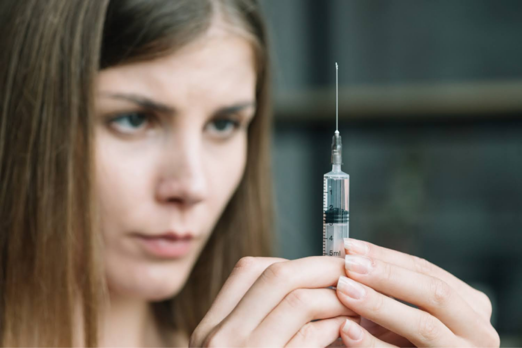 A woman carefully examining a syringe in preparation for use.