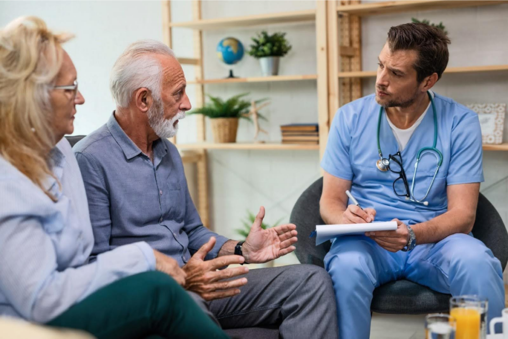 A doctor taking notes while speaking with an elderly couple during a medical consultation.