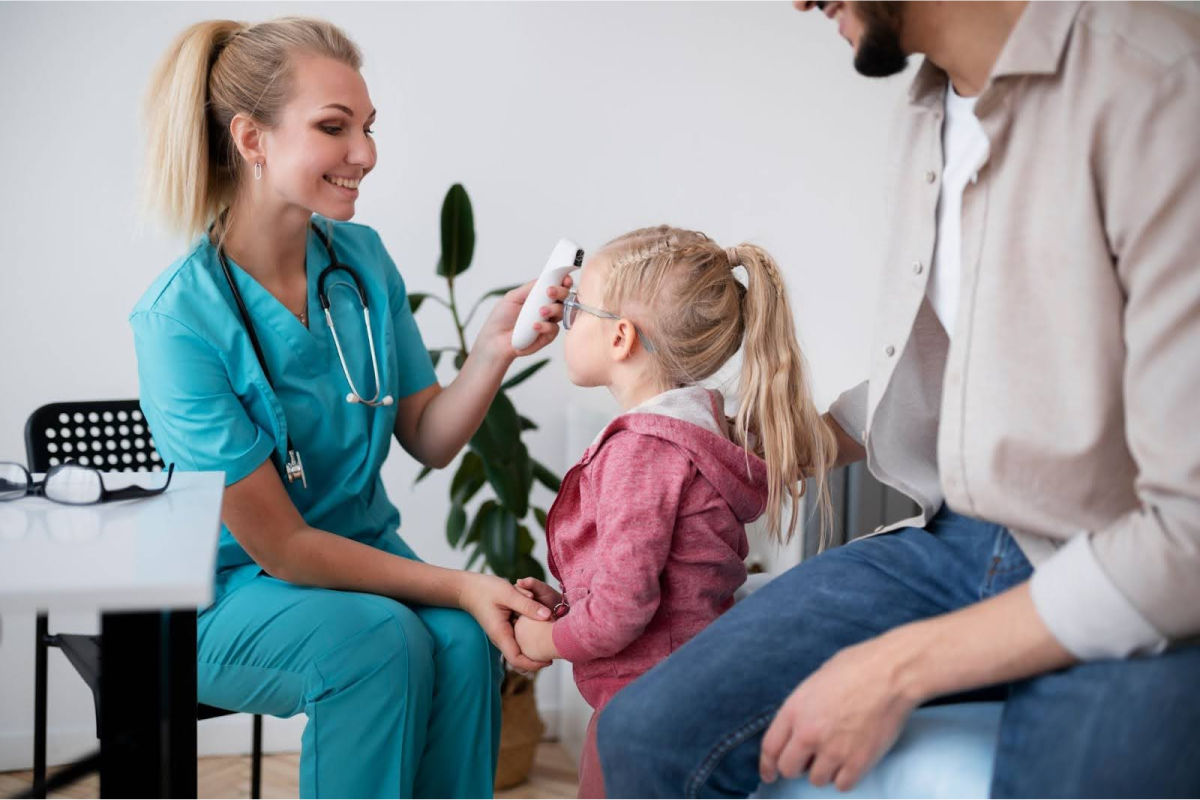 A nurse checking a young girl’s temperature with a forehead thermometer while the father sits nearby.