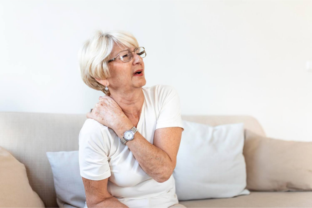 An elderly woman touching her shoulder, expressing discomfort.