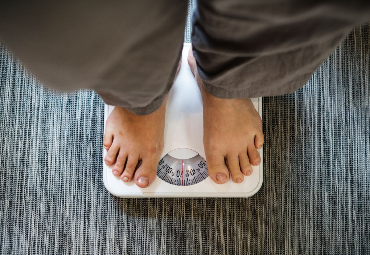 A person standing on a scale with a view of the weight dial on a tiled floor.