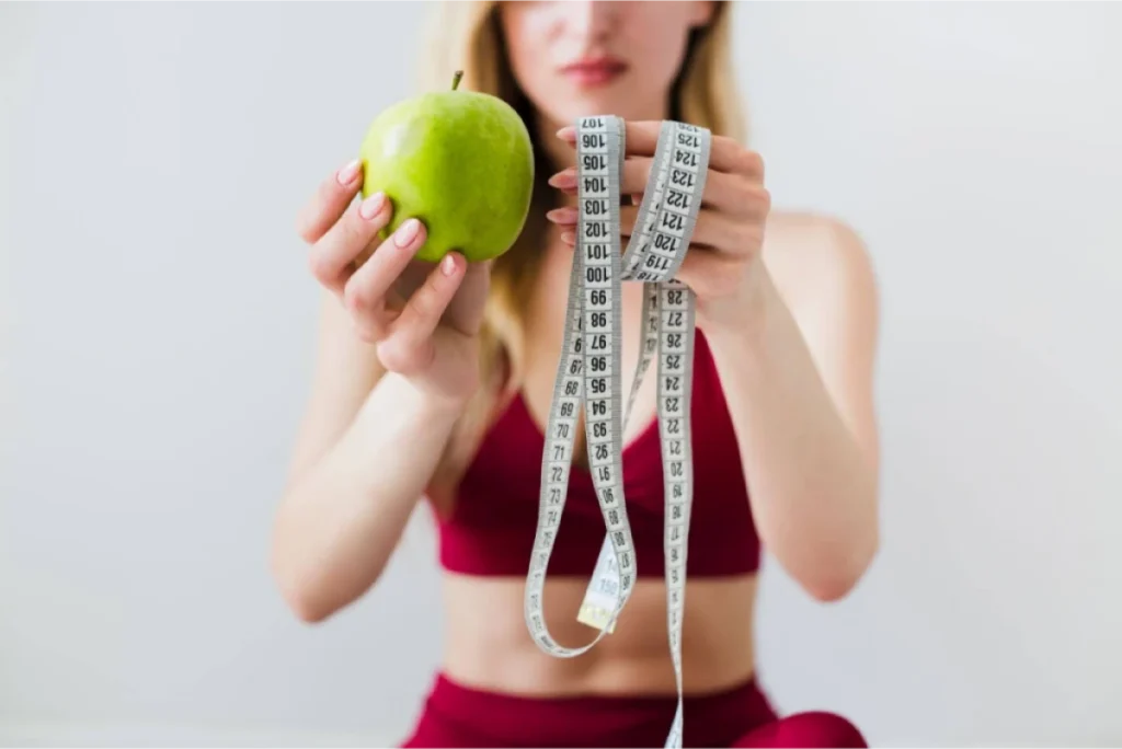 A woman holding a green apple and a measuring tape, symbolizing health and fitness.