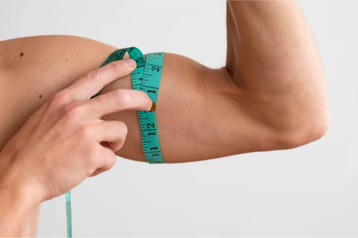 A person measuring their upper arm with a green measuring tape.