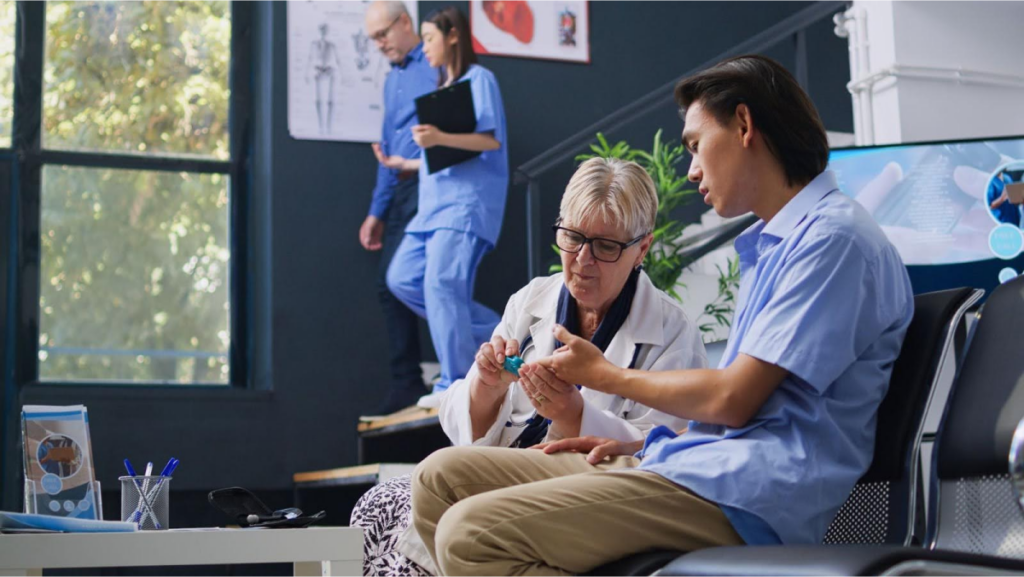 A doctor discussing medical equipment with a patient in a clinic setting, with other medical staff in the background.