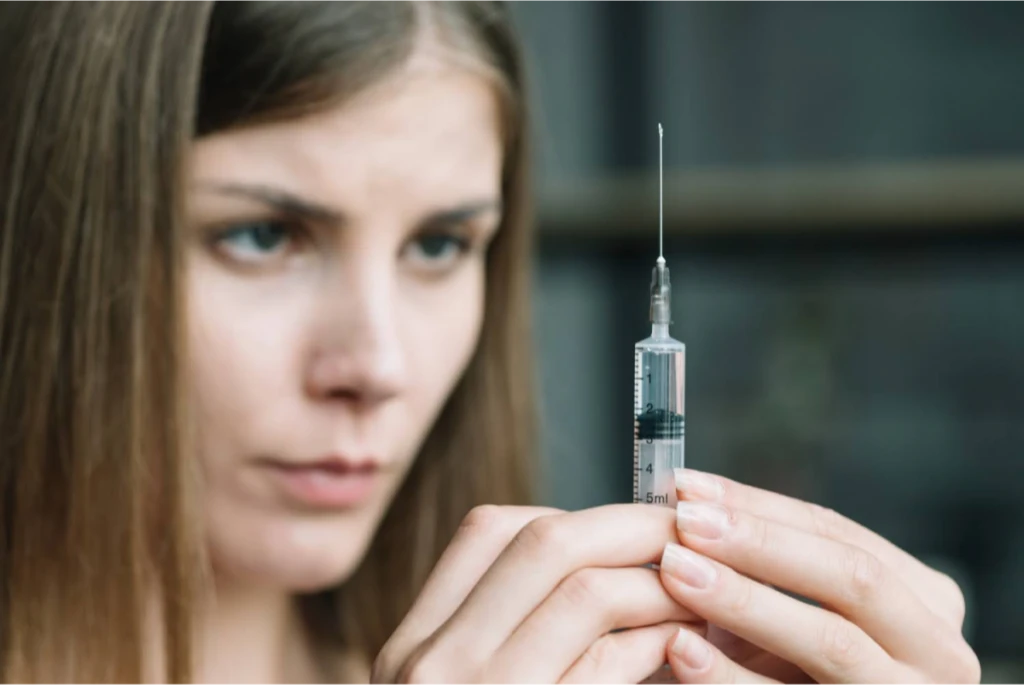 A woman carefully examining a syringe in preparation for use.