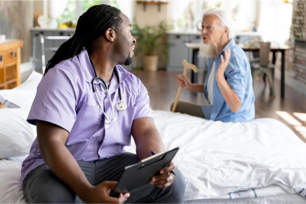 A healthcare worker speaking with an elderly woman who is holding a walking cane.