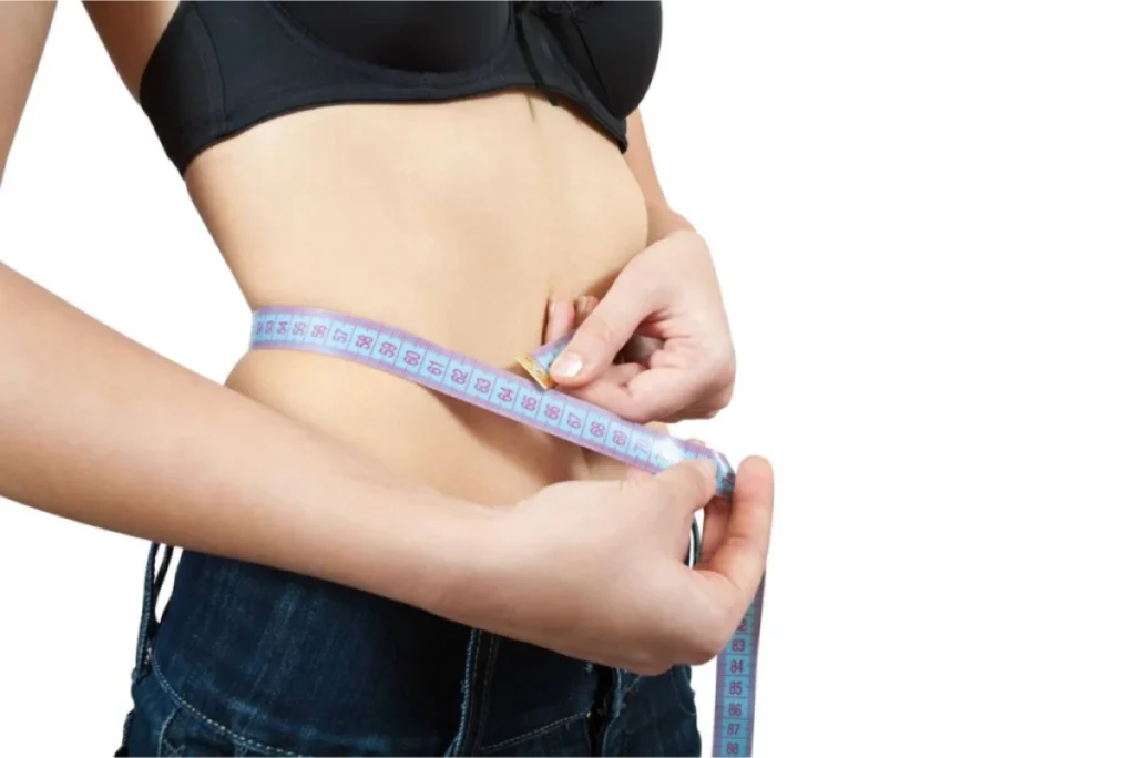 A person measuring their waist with a blue measuring tape while wearing jeans.