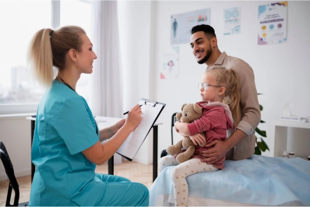 A nurse speaking with a young girl holding a stuffed toy, with her father sitting beside her.