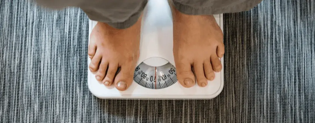 A person standing on a scale with a view of the weight dial on a tiled floor.