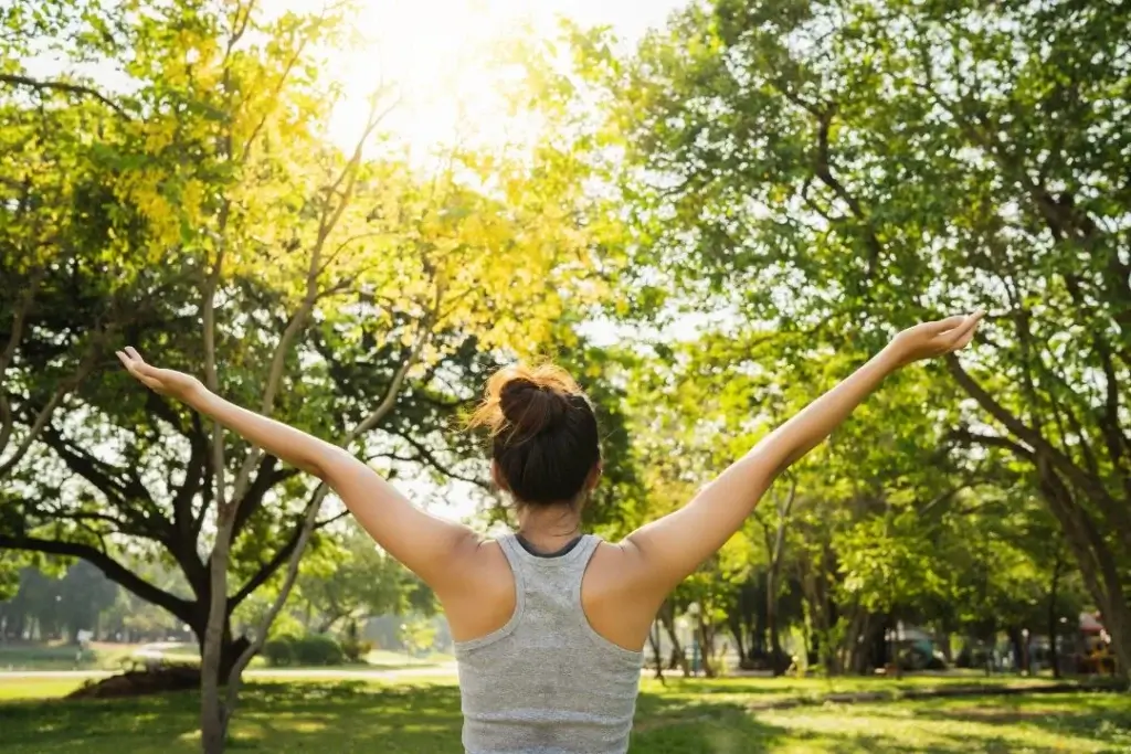 Woman standing in a park with arms outstretched, enjoying sunlight.