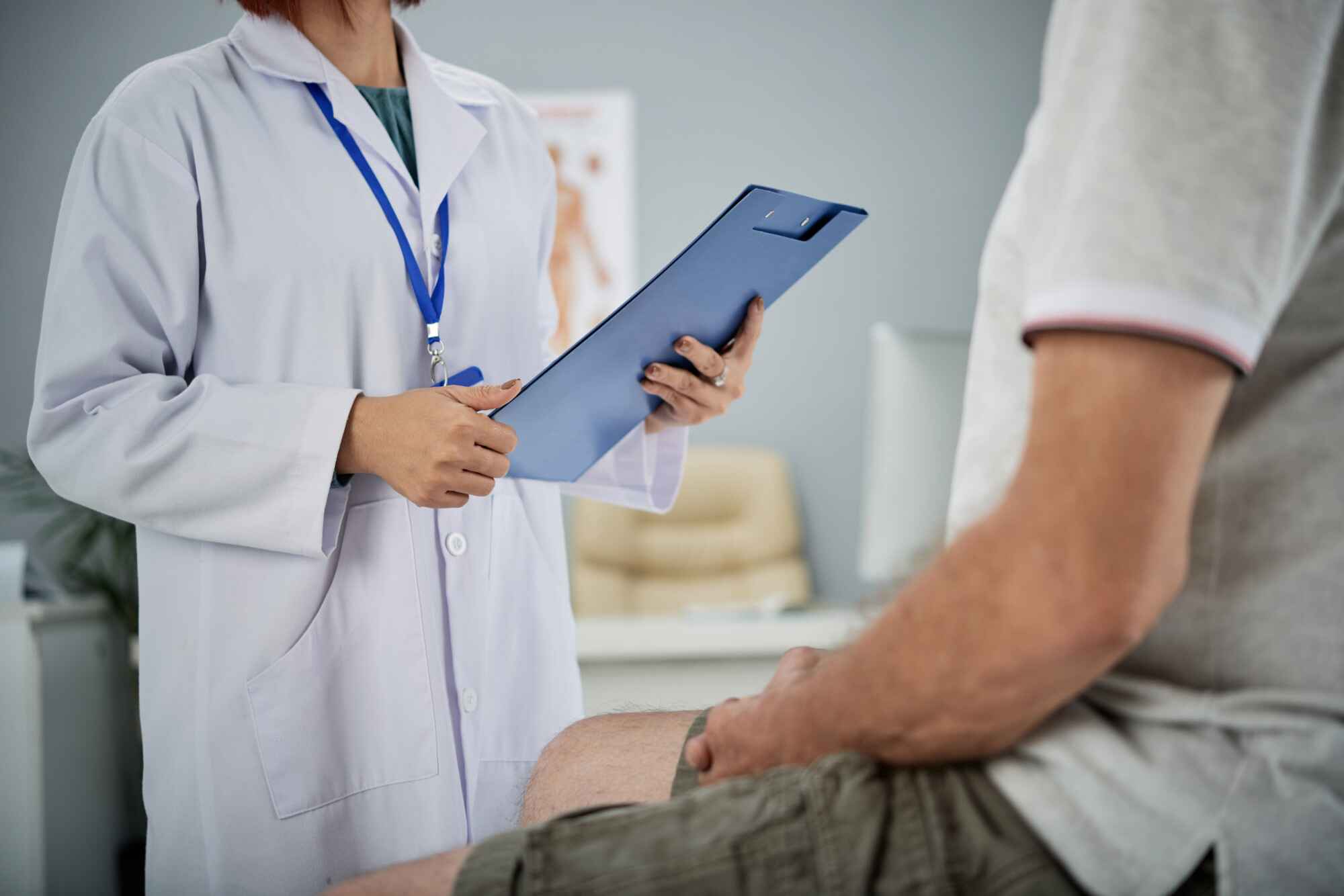 Doctor holding clipboard while patient sits.